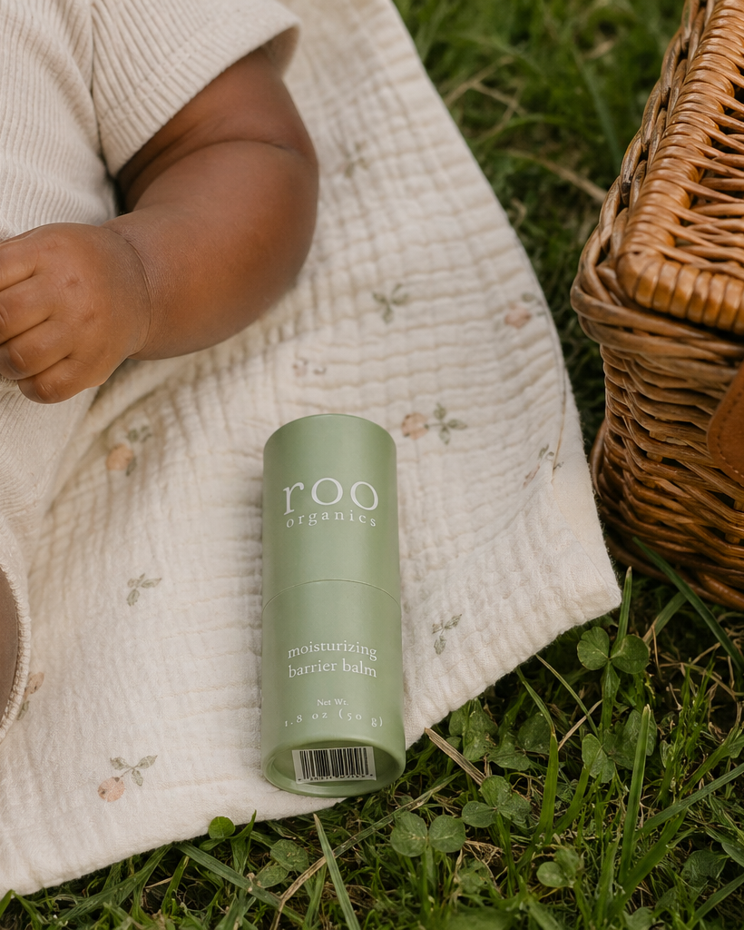 Child sitting on a blanket with a green bottle labeled 'roo' in a natural setting